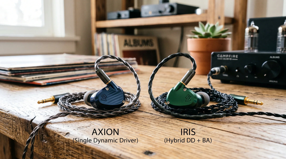 Side-by-side comparison of Campfire Audio Axion single dynamic driver IEMs and Iris hybrid dual-driver IEMs resting on a rustic wooden desk with audiophile equipment.